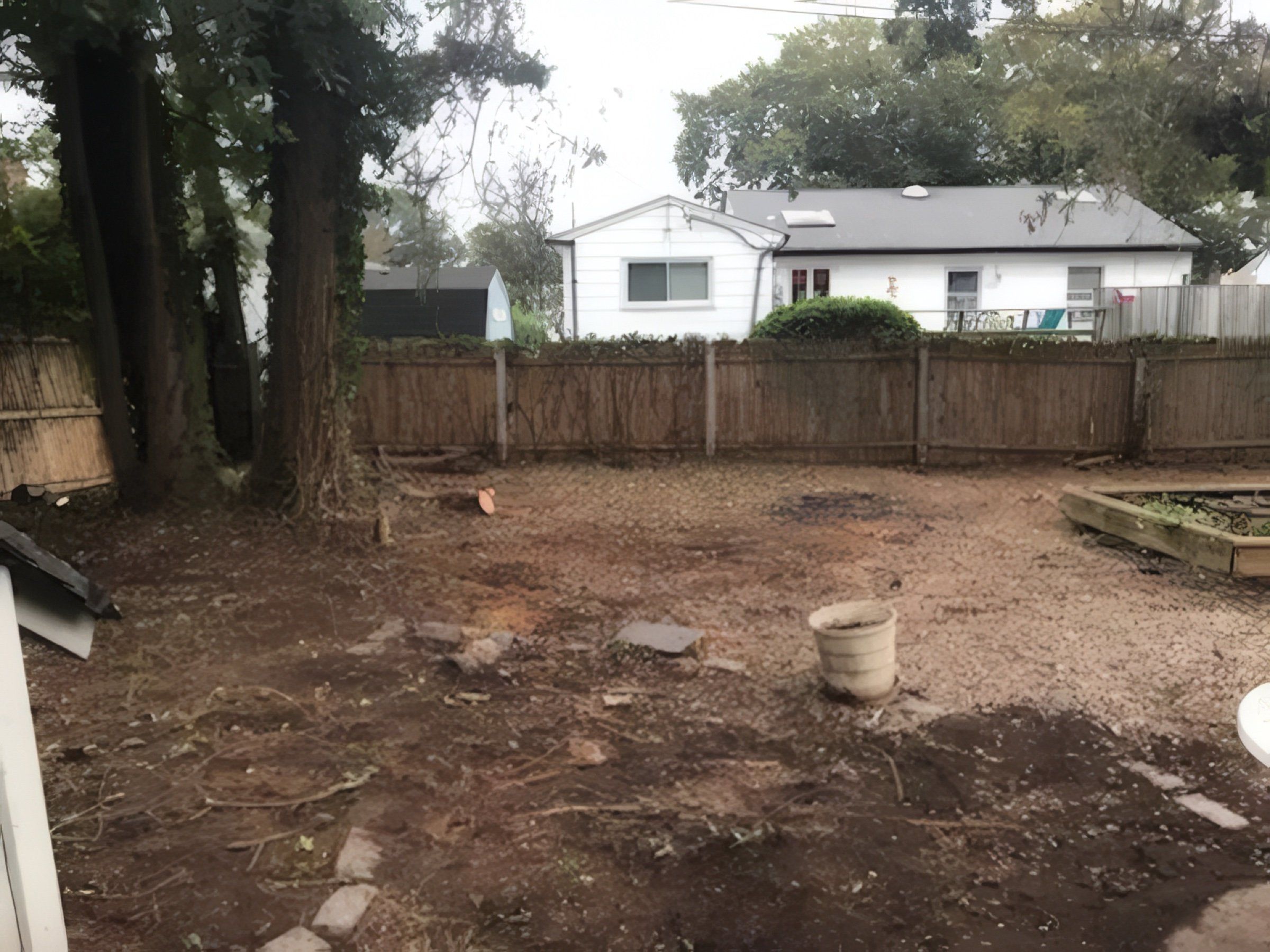 The backyard cleared to bare ground along a wood fence