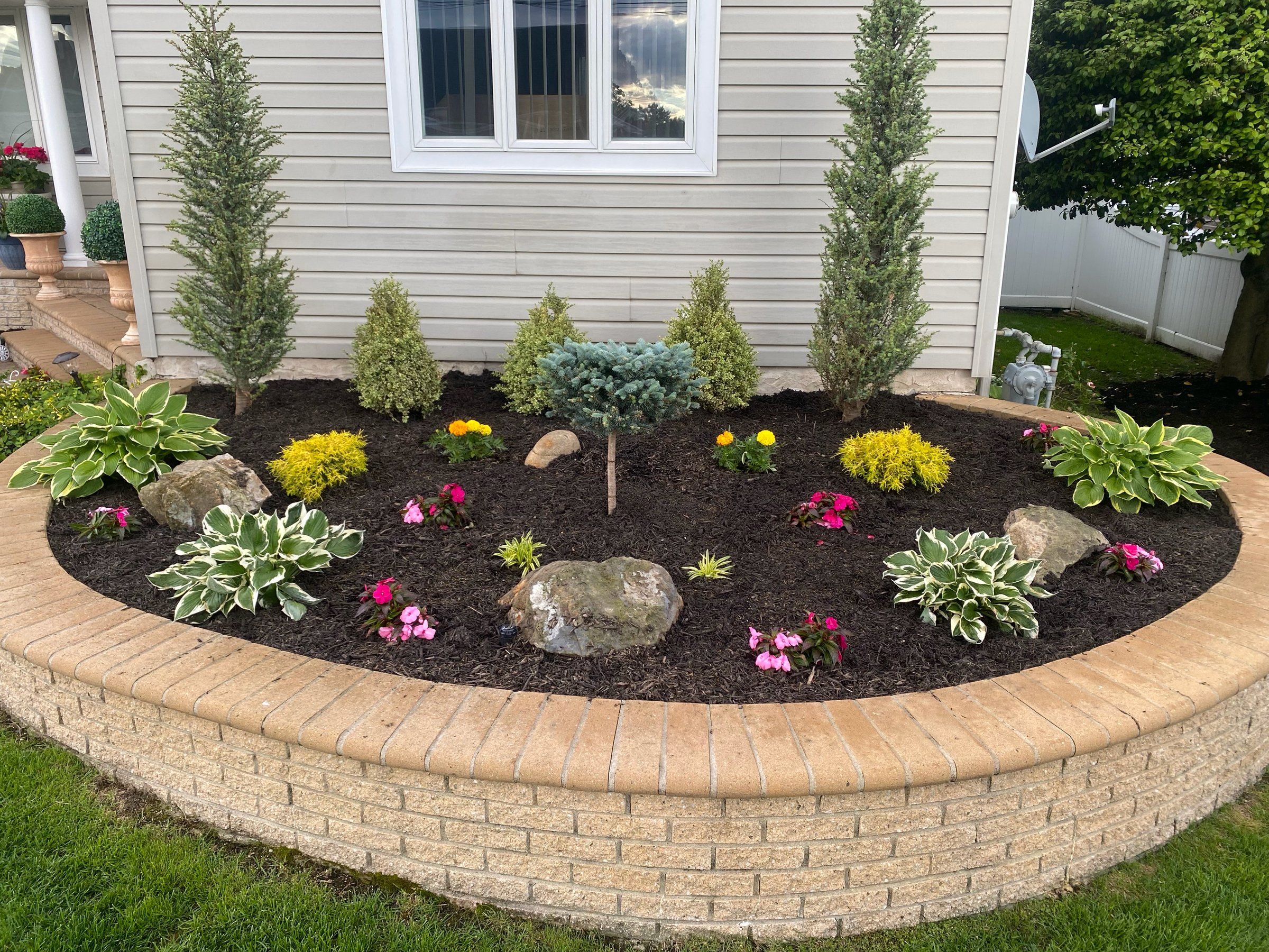 Raised bed finished with dark mulch, boulders, evergreens and annual flowers