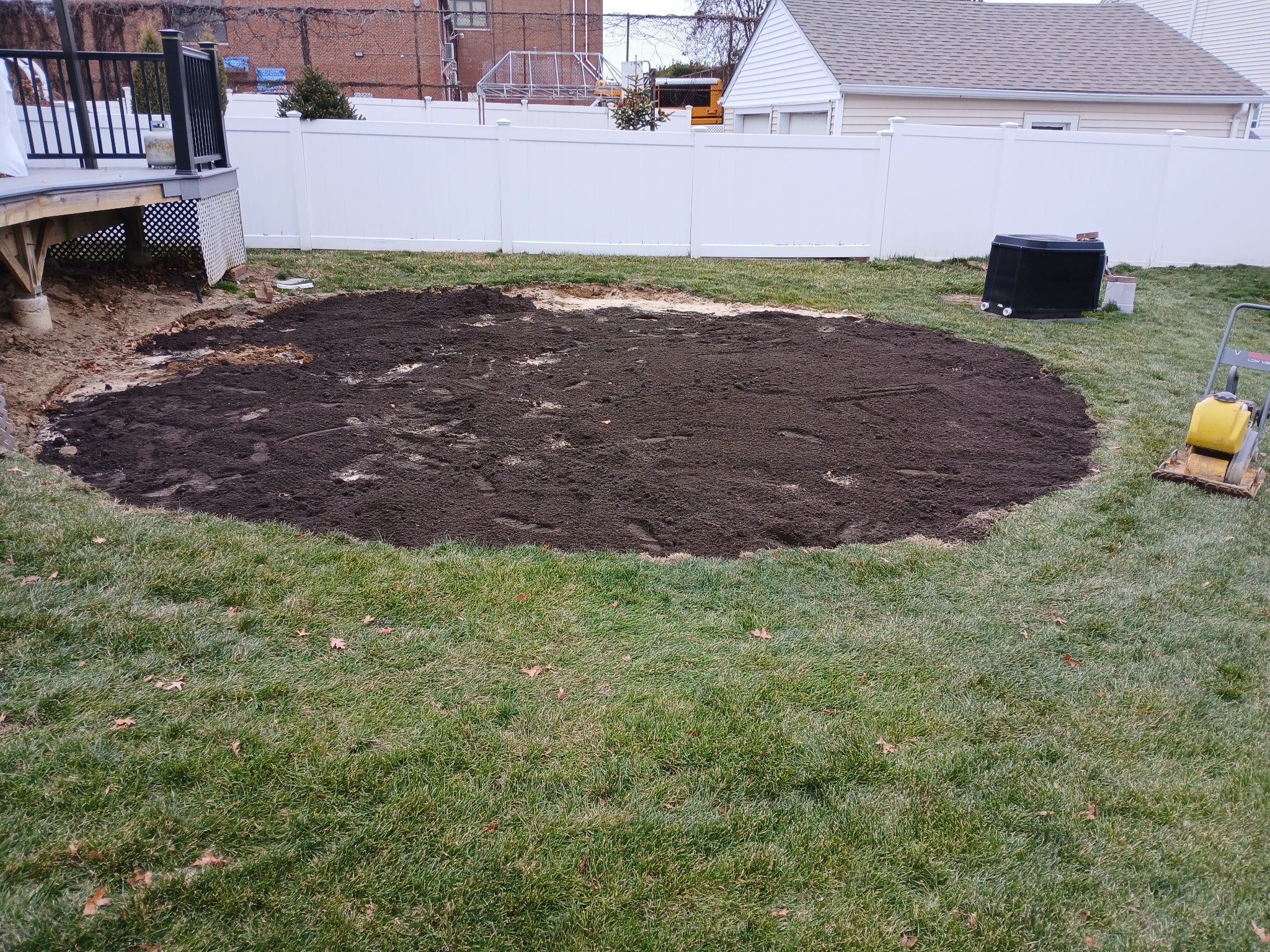 Round patch of graded topsoil in a fenced backyard lawn where a pool stood
