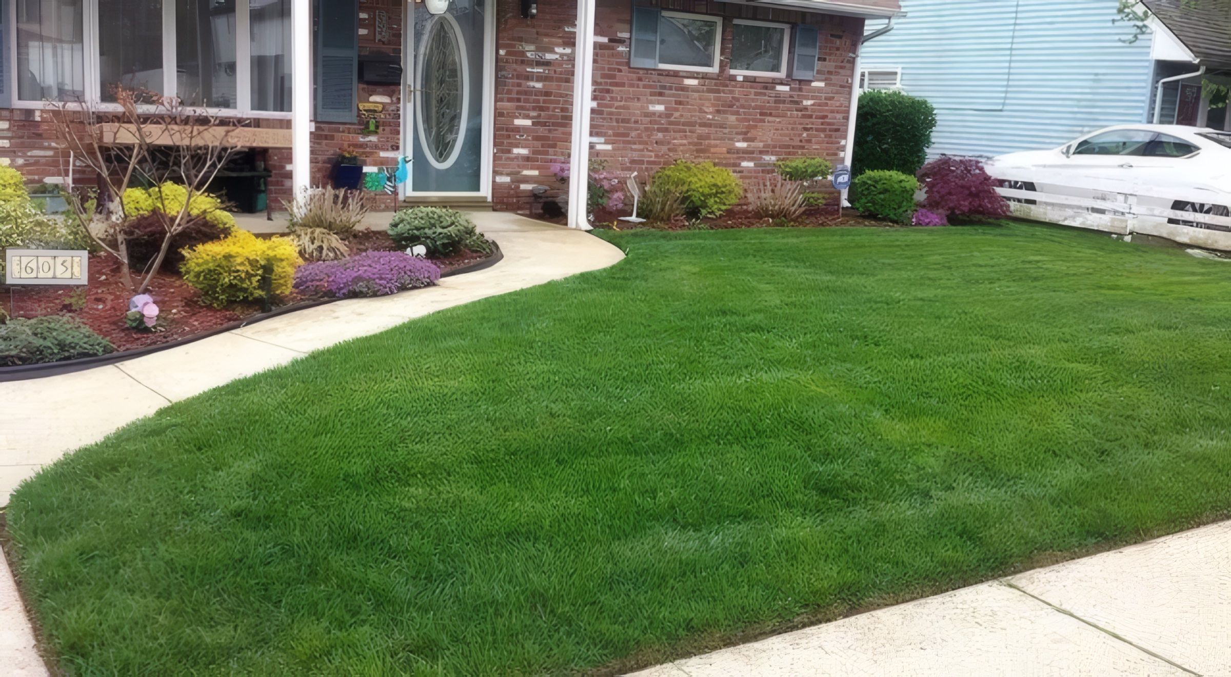 A mowed, striped front lawn beside trimmed beds at a brick house