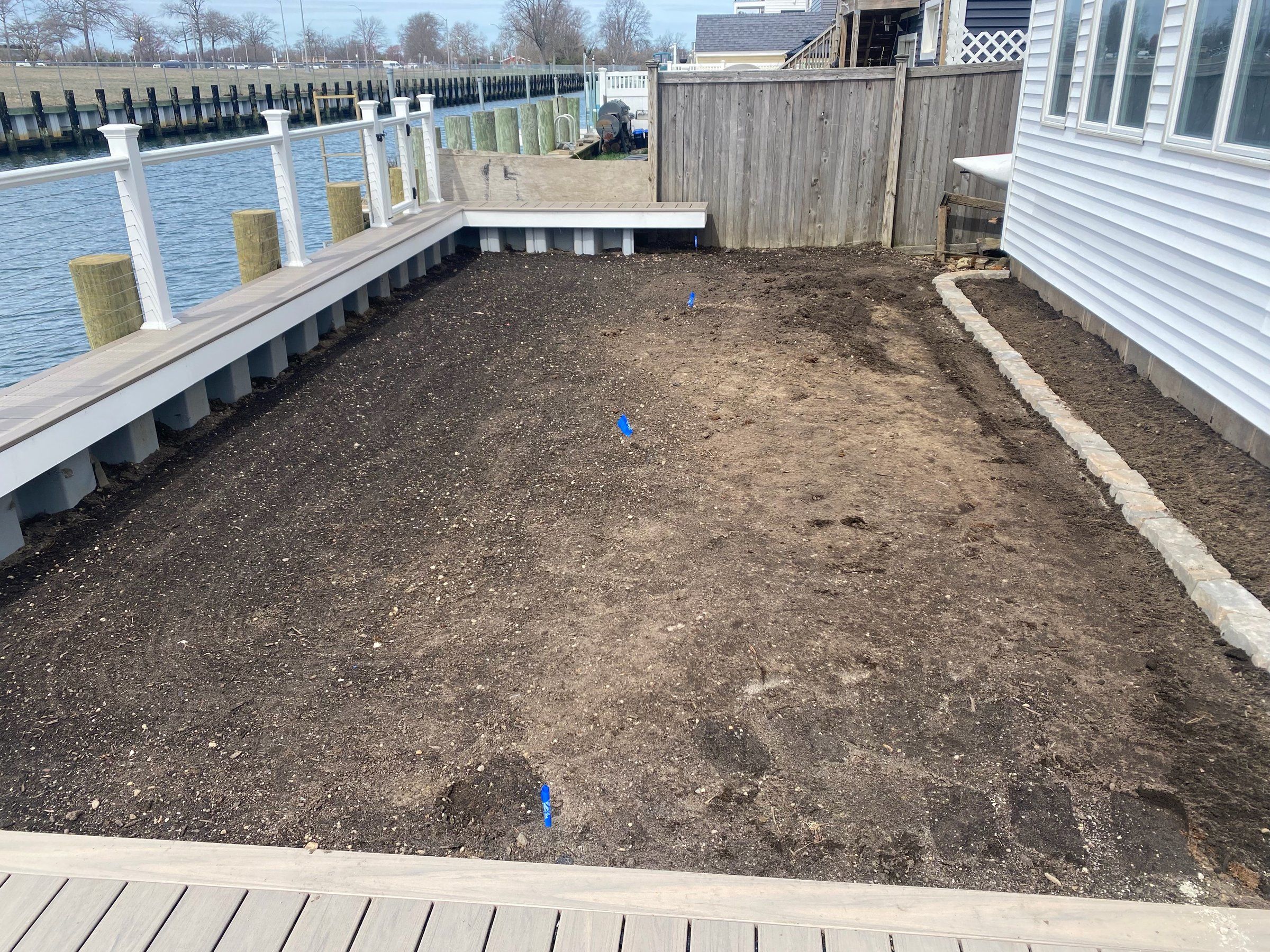 Side yard graded and leveled, with sprinkler flags in the soil and a new brick edge along the house